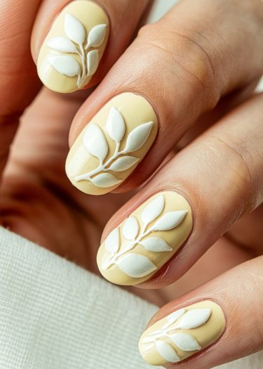 Elegant pastel yellow nail art with textured white leaf designs for a sophisticated look.