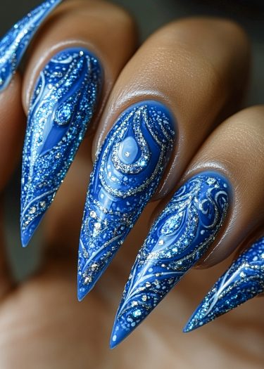 Elegant royal blue stiletto nails with intricate peacock feather designs and shimmering glitter accents.