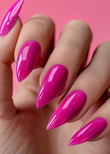 Vivid magenta stiletto acrylic nails on a well-groomed hand against a soft pink background.