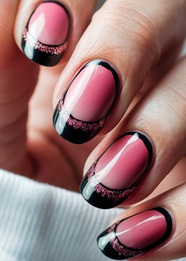 Elegant pink nails with black tips and glittery accents for a chic manicure.