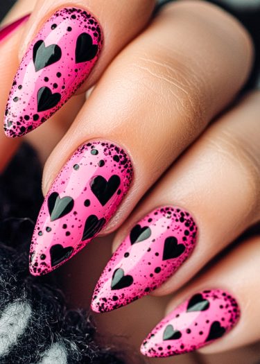 Vibrant pink stiletto nails with black heart designs and glossy finish for stunning nail art.