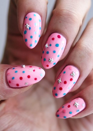 Vibrant pink manicure with playful polka dots and silver star embellishments on almond-shaped nails.