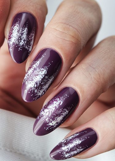 Elegant deep purple almond nails with artistic white splatters for a sophisticated look.