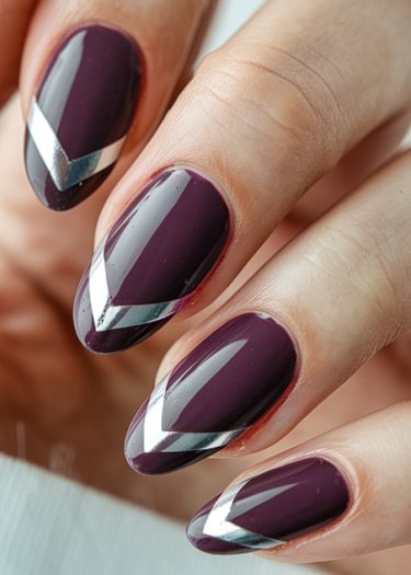 Elegant almond-shaped nails featuring rich plum polish and metallic silver chevron designs.