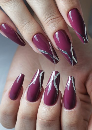 Elegant maroon stiletto nails with intricate silver designs for sophisticated nail art.