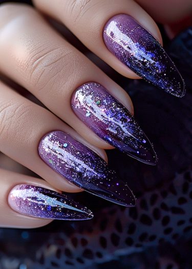 Exquisite purple to black gradient stiletto nails with sparkling glitter for a cosmic effect.