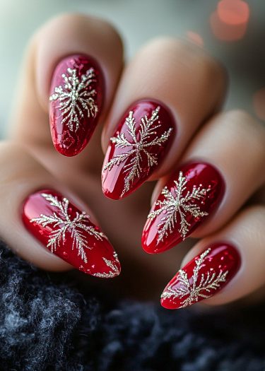 Elegant red almond nails adorned with gold snowflake designs and a cozy winter background.