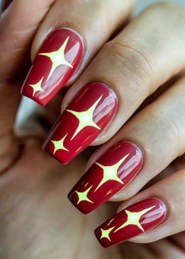 Elegant red nails with vibrant yellow star art for a stunning manicure look.