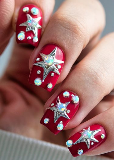 Vibrant red nails featuring 3D silver stars and radiant rhinestones for a glamorous look.