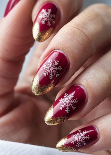 Elegant burgundy almond nails with gold tips and snowflake designs for a festive winter look.