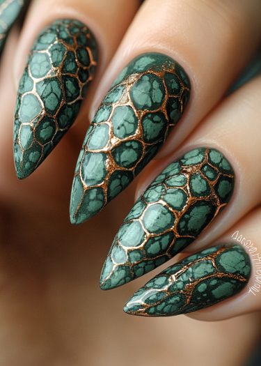 Stunning stiletto nails with green reptilian scales and metallic accents for bold nail art.