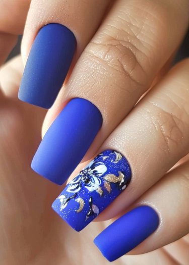 Elegant coffin-shaped cobalt blue nails with intricate floral art on the ring finger.