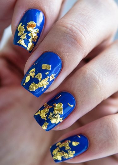 Elegant royal blue nails adorned with gold foil accents for a luxurious manicure look.