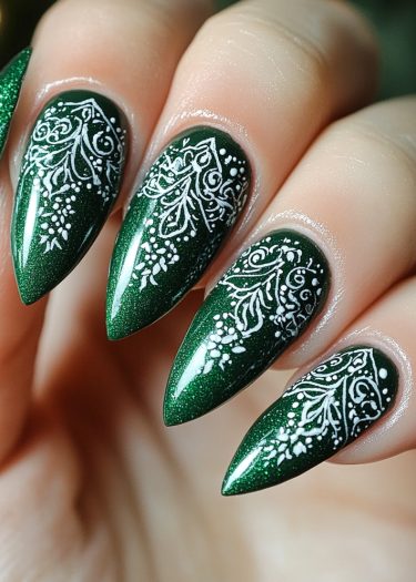 Elegant stiletto nails adorned with shimmering green polish and intricate white lace patterns.