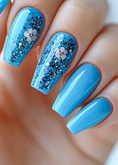 Elegant sky-blue coffin nails with floral designs and glitter for a chic manicure look.