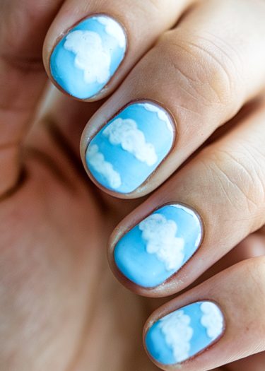 Vibrant sky-themed nail art with fluffy white clouds on a bright blue base.