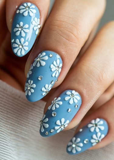 Elegant soft blue floral nail art with rhinestones on almond-shaped nails for a sophisticated look.