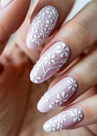 Elegant soft pink almond nails featuring intricate white floral nail art designs.