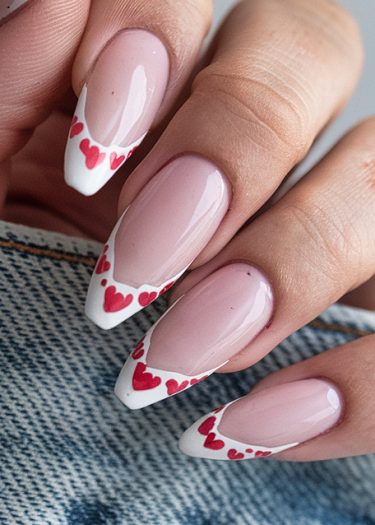 Elegant soft pink French tip nails with red heart accents on denim background.