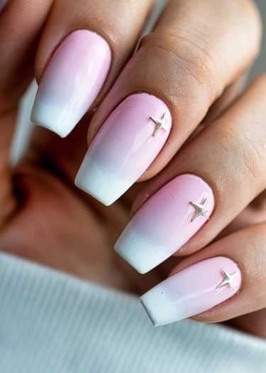 Stylish ombre pink and white nails with metallic star embellishments for an elegant look.