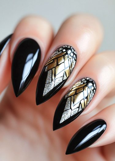 Elegant stiletto black nail art with gold and silver geometric designs and rhinestone accents.