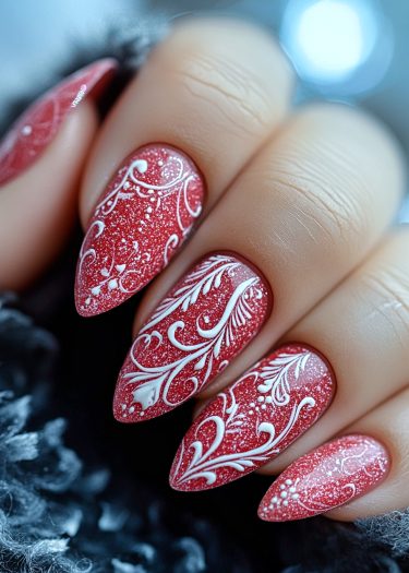 Elegant red nail art with intricate white designs and glittery accents on pointed almond nails.