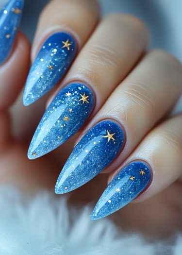 Elegant stiletto nails with starry night design, featuring blue ombre and glittery accents.