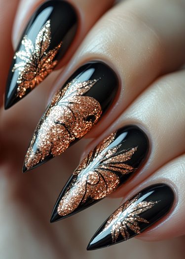 Glossy black stiletto nails with intricate copper glitter leaf designs for a bold look.