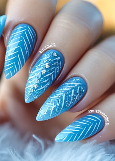 Elegant stiletto blue nail art with intricate white leaf patterns and subtle glitter accents.