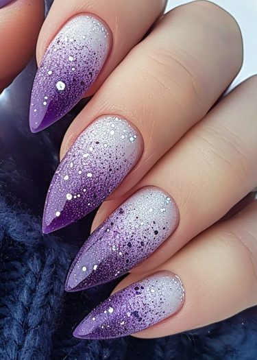 Elegant stiletto nails with purple ombre and sparkling accents on a textured blue background.