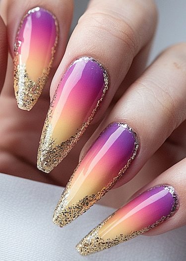 Elegant ombre stiletto nails in purple and gold with glitter accents for a glamorous look.