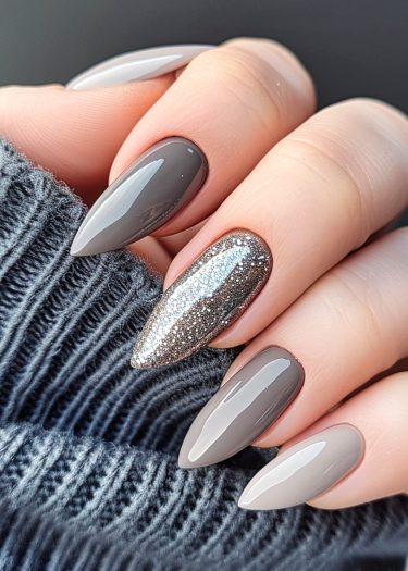 Elegant gray and silver glitter stiletto nails with cozy dark gray sweater background.