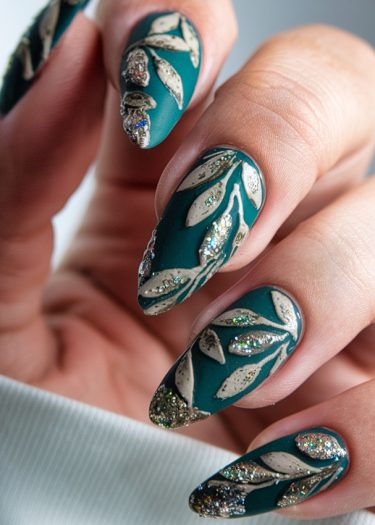 Elegant teal almond-shaped nails with intricate white foliage and shimmering glitter design.