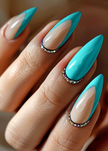 Bold turquoise stiletto nails with glitter accents and a nude base for a chic manicure.