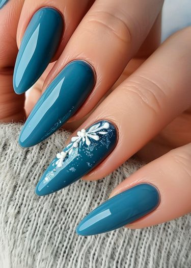 Elegant teal stiletto nails with floral nail art on textured fabric background.