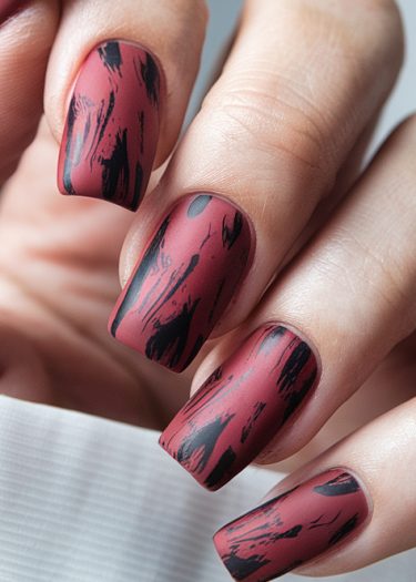 Artistic burgundy nails with black brushstrokes, showcasing trendy matte manicure design.