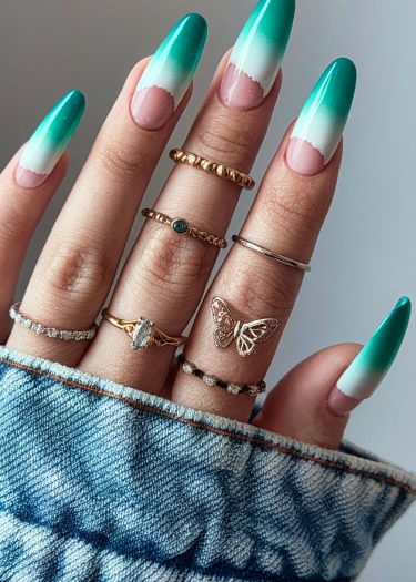 Turquoise ombre nail art with stylish rings on a denim background.