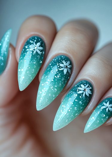 Elegant turquoise ombre stiletto nails with floral designs and shimmering glitter accents.