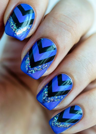 Vibrant blue nails with black chevron stripes and sparkling glitter for a bold, modern look.