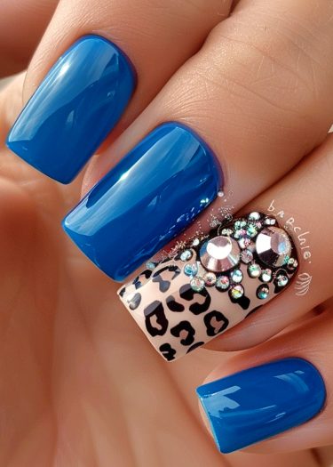 Vibrant blue nail art with leopard print and rhinestones for a stylish manicure.