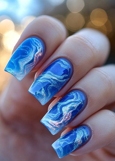 Stunning blue nail art with marbling and glitter on elegantly manicured square tips.