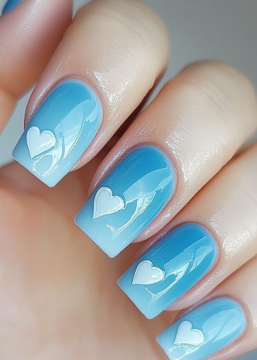 Vibrant blue gradient nails with 3D white hearts for a stylish and modern manicure.