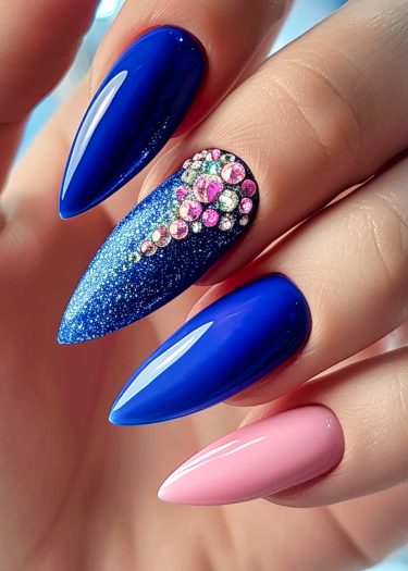 Elegant stiletto nails with vibrant blue and soft pink designs, featuring glitter and rhinestones.