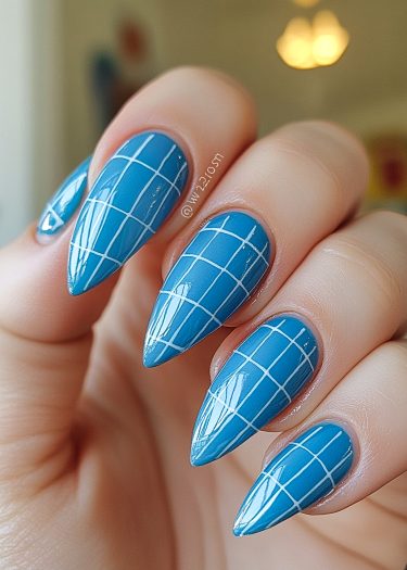 Vibrant blue stiletto nails with a chic white grid pattern for a modern manicure style.