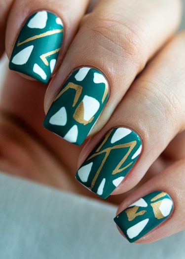 Stylish teal geometric nail art with white and gold accents on manicured nails.