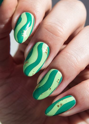 Elegant green nail art with gold leaf embellishments, showcasing intricate designs and modern style.