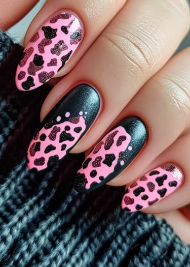 Stylish pink and black leopard print nail art on manicured almond-shaped nails against textured fabric.