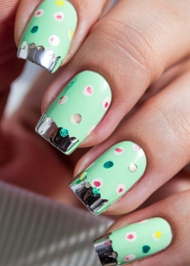 Elegant mint green nail art with colorful polka dots and metallic silver tips.