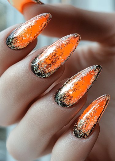 Stunning vibrant orange stiletto nails with gold glitter for a glamorous nail art look.