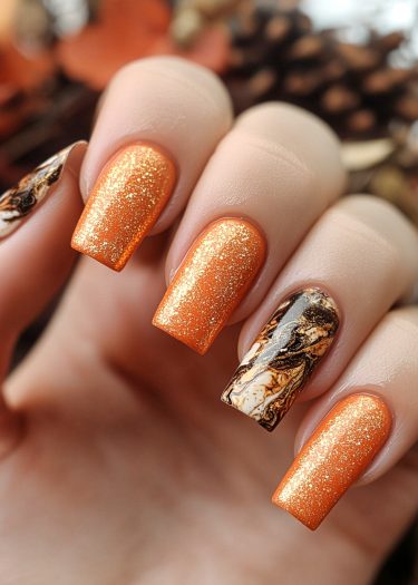 Autumn-inspired vibrant orange glitter nails with elegant marble design on ring finger.